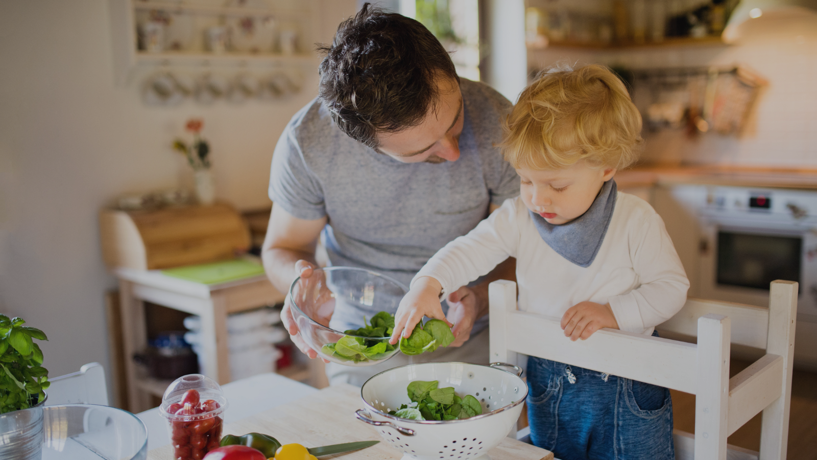 Father helping his 2 year old toddler prepare food in the kitchen as part of simple learning activities at home